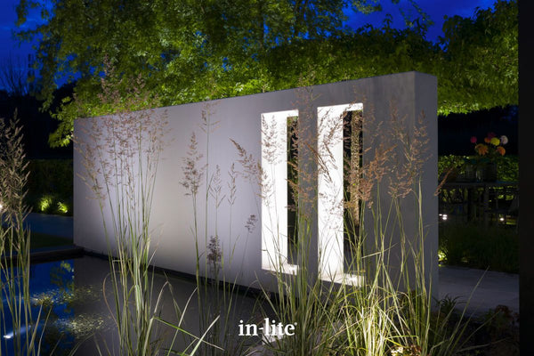 Atmospheric lighting by in-lite. BIG FLUX ASYMMETRIC 12v outdoor ground recessed light fixtures projecting elongated, shaped light beams within architectural wall recesses, illuminating the facades within.