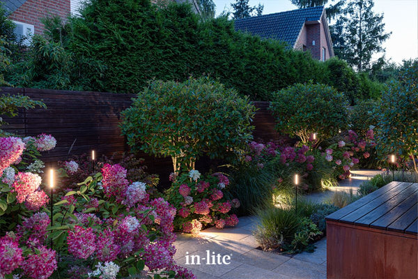 Atmospheric lighting by in-lite. BREEZE and BREEZE LOW 12v Outdoor COB LED strip light flexible 360 degree lighting fixtures positioned between plants, illuminating in and around perennials and grasses in planted borders in contemporary landscape.