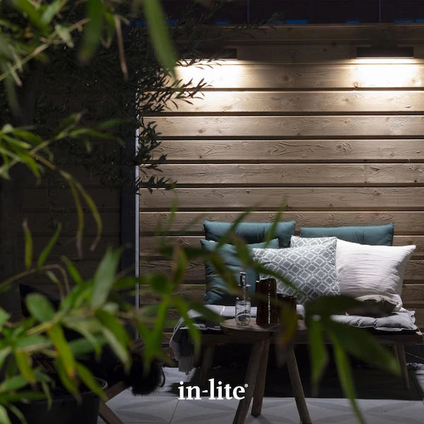 in-lite atmospheric garden lighting. in-lite EVO DOWN Dark 12v outdoor wall lights installed on wooden wall section. The dark coloured, slim wall lights are illuminating the wall facade and patio space with a focused ambient washes of light.