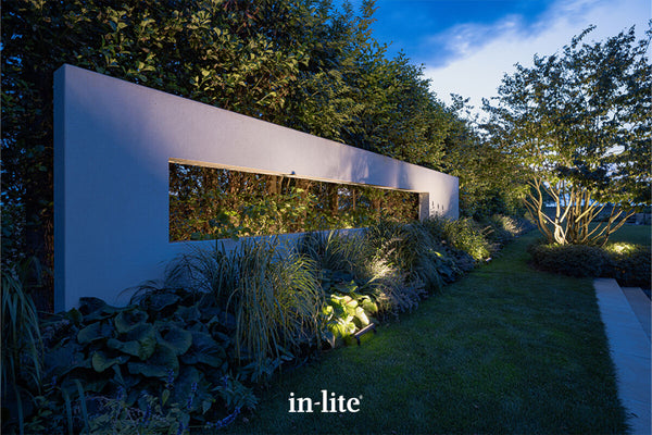 Atmospheric lighting by in-lite. EVO FLOOD 12v outdoor floodlighting fixtures illuminating architectural wall features with targeted wide light beams in a maturely landscaped border.