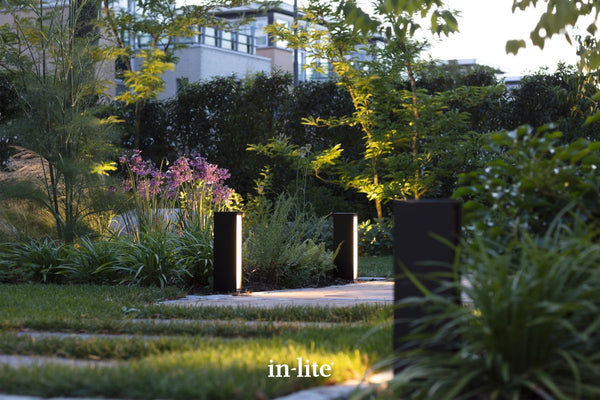 Atmospheric lighting by in-lite. EVO LOW DARK 12v outdoor architectural bollards, positioned in borders, illuminating along a pathway in a contemporary landscape.