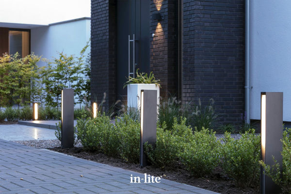 Atmospheric lighting by in-lite. EVO DARK 12v outdoor architectural bollards, positioned in pathway border, illuminating diffused light along paved driveway in modern landscape.