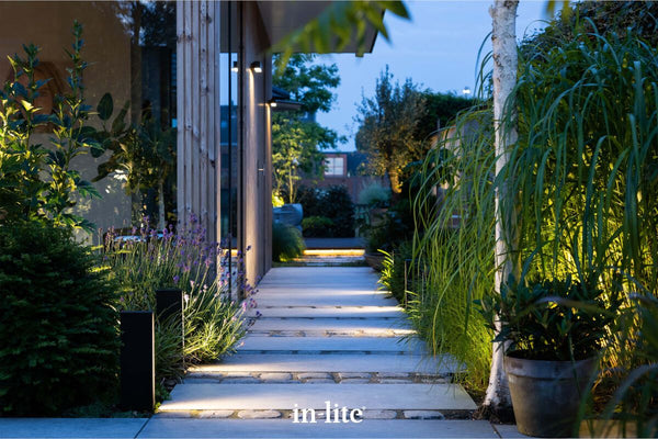 Atmospheric lighting by in-lite. EVO DARK 12v outdoor architectural bollards, positioned in pathway border, illuminating diffused light along stone pathway in modern landscape.