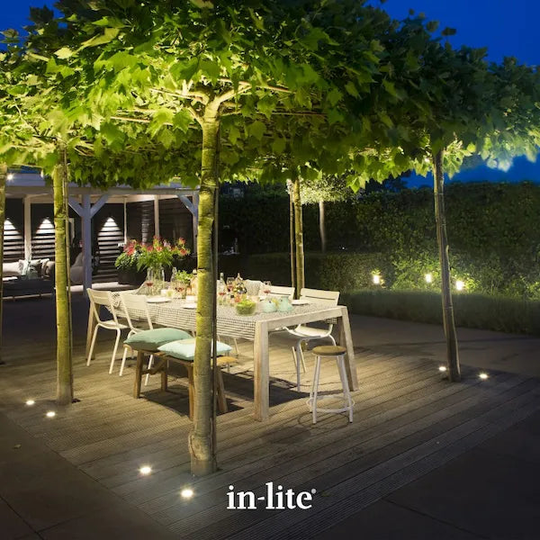 in-lite atmospheric garden lighting. In-lite FLUX 12v Outdoor Spotlights installed in ground positions around decking borders. The In-lite FLUX ground spotlights are illuminating trunks and canopies of horizontal pleached trees planted in and around the decking borders of an Alfresco dining space.