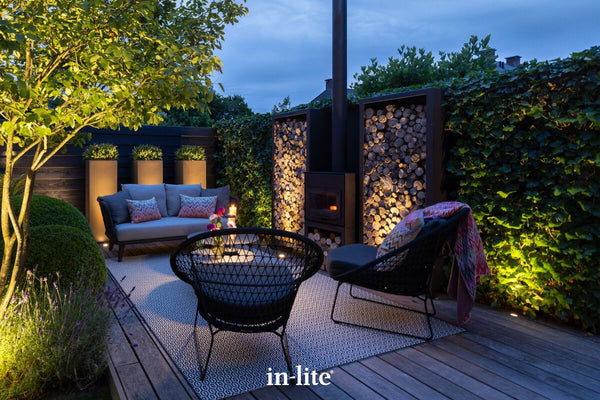 Atmospheric lighting by in-lite. FLUX 12v outdoor ground recessed light fixtures illuminating elements around the perimeter space of a deck with lounge table and seating.