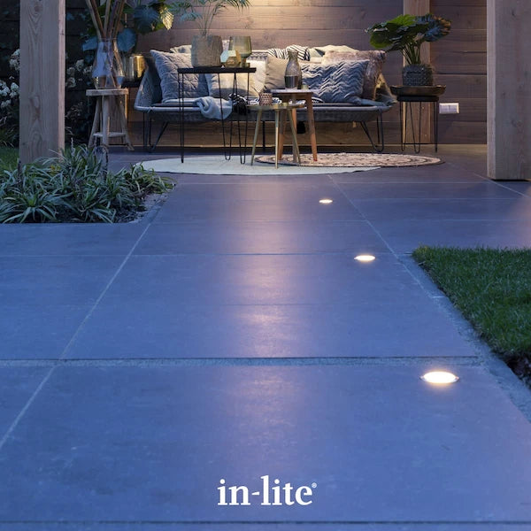 in-lite atmospheric garden lighting. In-lite FUSION 12v Outdoor ground lights recessed in stone paving tiles along patio walkway. In-lite FUSION 12v Outdoor ground lights are installed in the pavers with a stainless steel ring resting at the surface. The stone paving tile is illuminated indicatively by the soft ambient glow of the In-lite FUSION 12v Outdoor ground lights installed along the patio walkway.