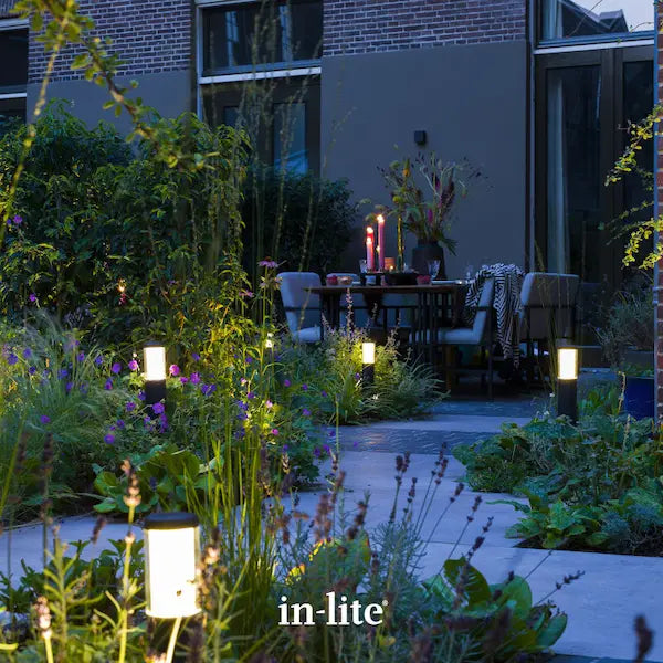 in-lite atmospheric garden lighting. in-lite LIV DARK 12v outdoor post lights positioned in patio borders with shrubs and plants. The dark coloured, tall and slim light fixtures are illuminating around the patio borders and pathways with soft ambient light.