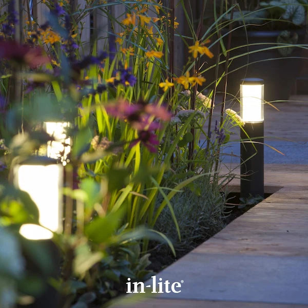 in-lite atmospheric garden lighting. in-lite LIV LOW DARK 12v outdoor post lights positioned in patio border with shrubs and plants. The dark coloured, slim and low level light fixtures are illuminating around the patio border and walkway with soft ambient light.