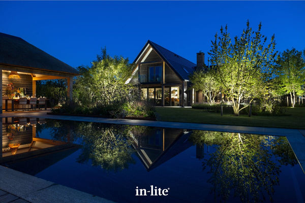 Atmospheric lighting by in-lite. SCOPE 12v outdoor spotlight fixtures illuminating deciduous trees with rounded canopies and low-branching trunks. The landscape lighting and the reflection in the pool are incredible, creating a night shot with dramatic uplighting in balanced and landscaped grounds of a premium property.