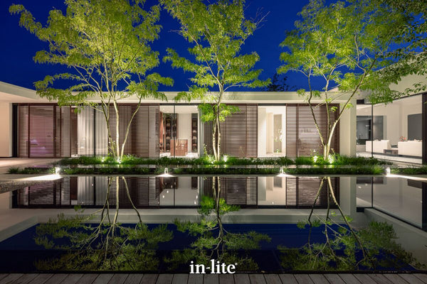 Atmospheric lighting by in-lite. SCOPE 12v outdoor spotlight fixtures illuminating Thornless Honey Locust trees. The branches arch gracefully and the incredibly fine, fern-like leaves catch the uplighting without creating dense, heavy shadows. The trees are used to frame the modern architecture and pool in a fantastic, straight-on view of a modern courtyard.