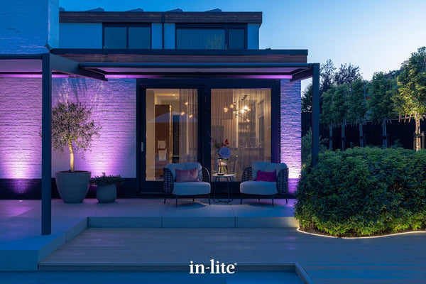 Atmospheric lighting by in-lite. SMART FLUX TONE 12v outdoor ground recessed vertical lighting fixtures washing exterior wall facades with vibrant colours along a modern and luxurious terrace outdoors.