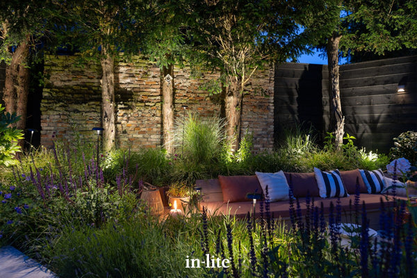 Atmospheric lighting by in-lite. SWAY 12v outdoor lighting fixtures illuminating border shrubs and perennials. Mature conifer trees and brick visual walls illuminated from ground spotlights in traditionally landscaped garden.