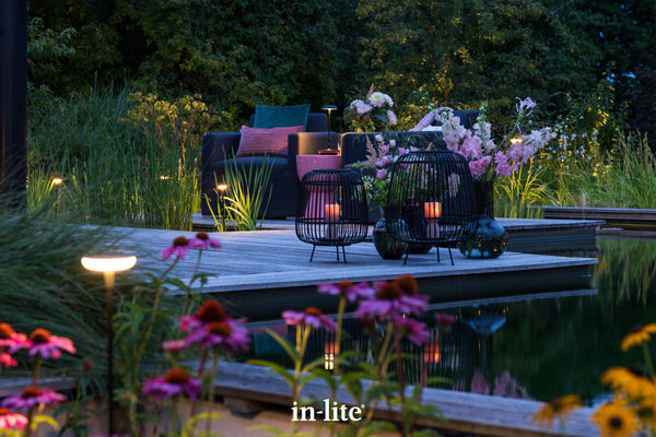 Atmospheric lighting by in-lite. SWAY 12v outdoor bollard light fixtures illuminating flowering perennials harmoniously in borders around waterside decking walkways and outdoor seating area.